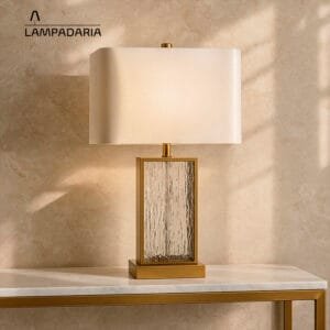 Abajur de vidro com detalhes em metal com cúpula branca sobre uma mesa branca com pés metálicos dourados