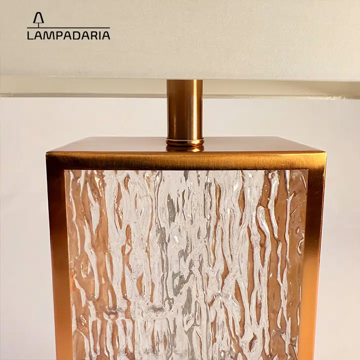 Abajur em vidro artesanal transparente e latão dourado com pantalha retangular em tecido algodão mercerizado brilhante na cor off-white.
