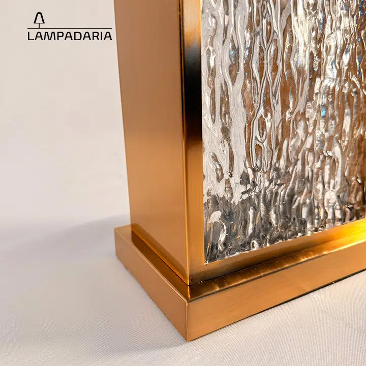 Abajur em vidro artesanal transparente e latão dourado com pantalha retangular em tecido algodão mercerizado brilhante na cor off-white.