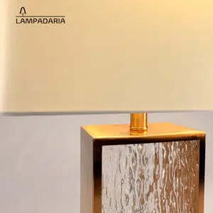 Abajur em vidro artesanal transparente e latão dourado com pantalha retangular em tecido algodão mercerizado brilhante na cor off-white.