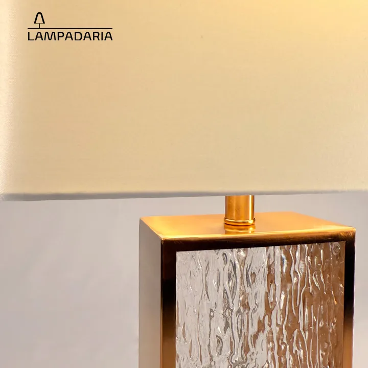Abajur em vidro artesanal transparente e latão dourado com pantalha retangular em tecido algodão mercerizado brilhante na cor off-white.