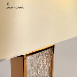 Abajur em vidro artesanal transparente e latão dourado com pantalha retangular em tecido algodão mercerizado brilhante na cor off-white.