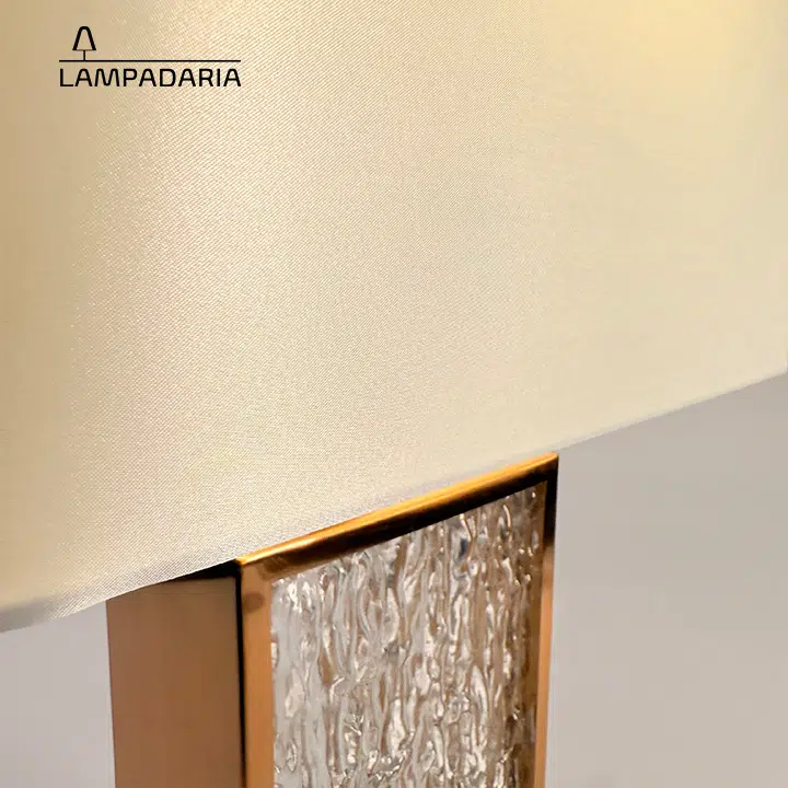 Abajur em vidro artesanal transparente e latão dourado com pantalha retangular em tecido algodão mercerizado brilhante na cor off-white.