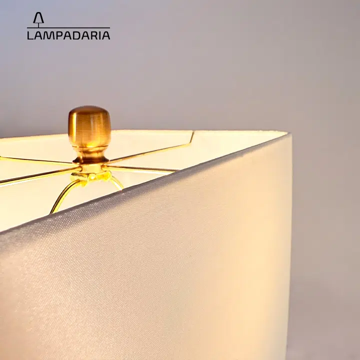 Abajur em vidro artesanal transparente e latão dourado com pantalha retangular em tecido algodão mercerizado brilhante na cor off-white.