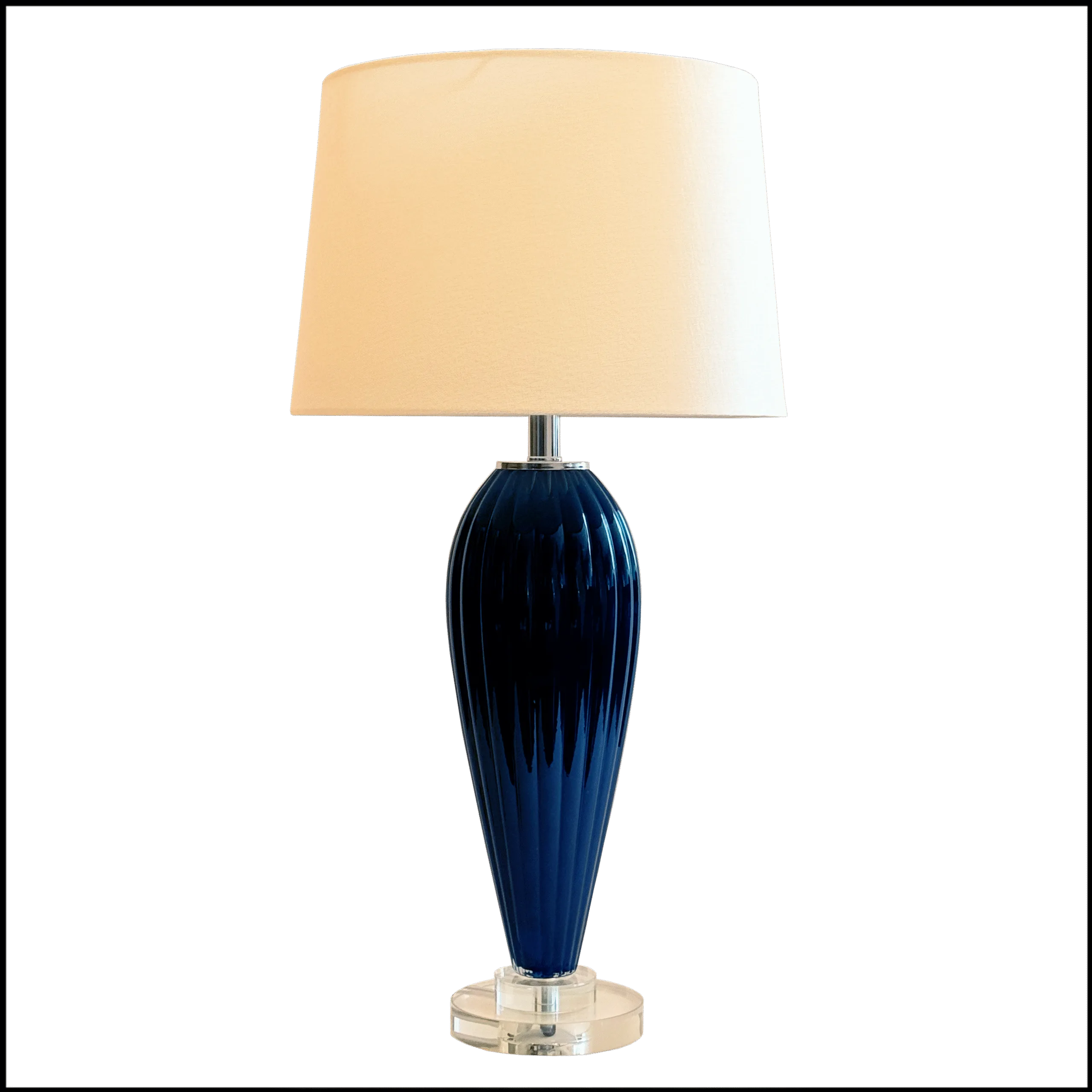 O Abajur Nightglass da Lampadaria é a perfeita fusão entre design clássico moderno, brilho e sofisticação. Sua base alta, em cristal azul noite moldada no formato de balaústre com frisos boleados e detalhes em cristal transparente, adiciona um toque de requinte e elegância ao ambiente. A cúpula translúcida em tecido algodão texturizado na cor branca distribui a luz uniformemente para cima e para baixo, criando uma atmosfera acolhedora, enquanto difunde lateralmente, contribuindo para a iluminação geral do espaço.